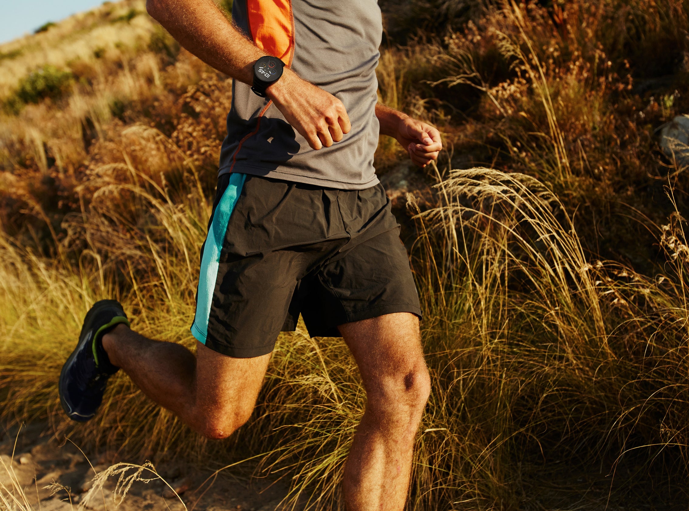Person running on a trail with grass and natural light wearing smartwatch