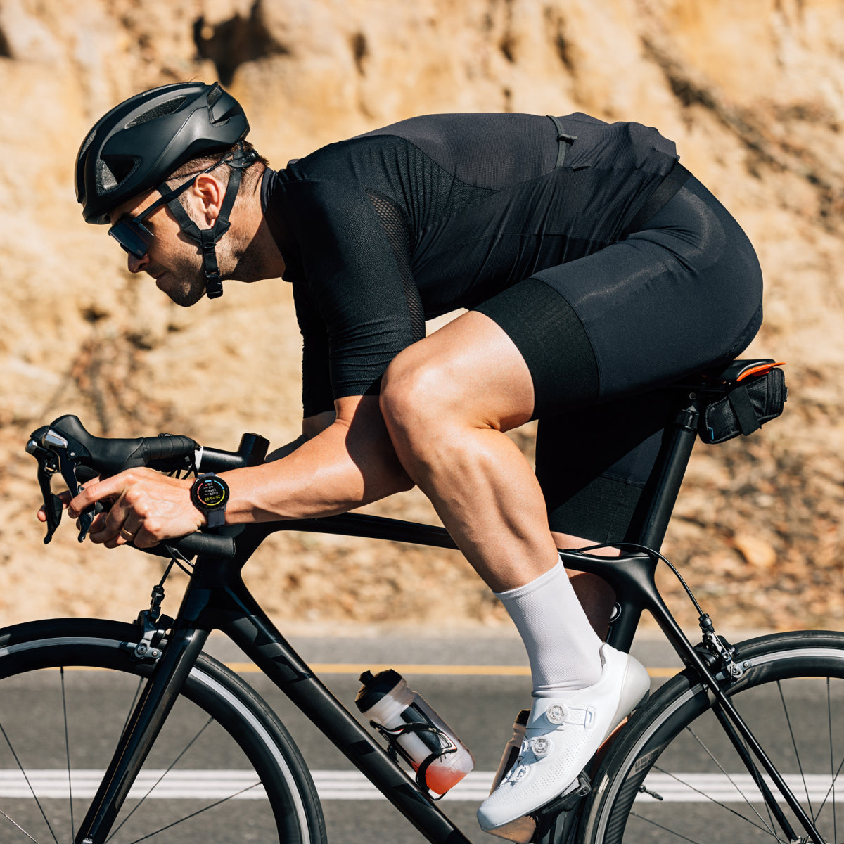 Cyclist in black gear riding a bike on a road with a blurred natural background wearing smartwatch